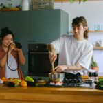 woman taking a picture of a man cooking in a kitchen