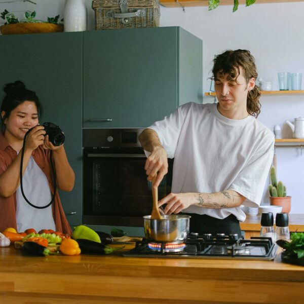 woman taking a picture of a man cooking in a kitchen