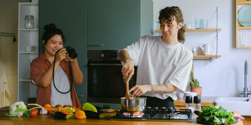 woman taking a picture of a man cooking in a kitchen