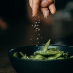 person pouring seasoning on green beans on bowl