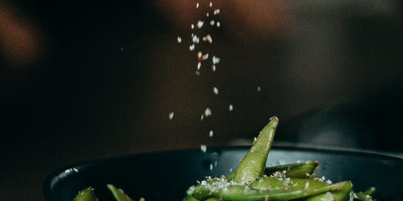 person pouring seasoning on green beans on bowl