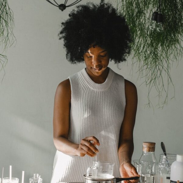 tranquil black woman making candles on cooker in workshop